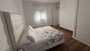 A bedroom with a bed, a window with curtains, a door, and a wall-mounted air conditioning unit. - El Balcón          . (Algodonales)