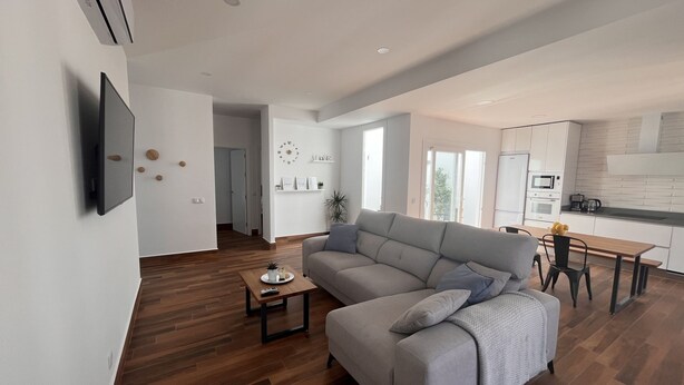 A modern living room with a grey sofa, wooden flooring, a small coffee table, and a TV mounted on the wall. - El Balcón          . (Algodonales)