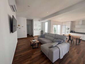 Una sala de estar moderna con un sofá gris, suelo de madera, una mesita de centro y un televisor montado en la pared.