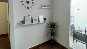 A modern living room with a wooden floor, a large wall clock, and decorative shelves with framed items and a potted plant. - El Balcón          . (Algodonales)