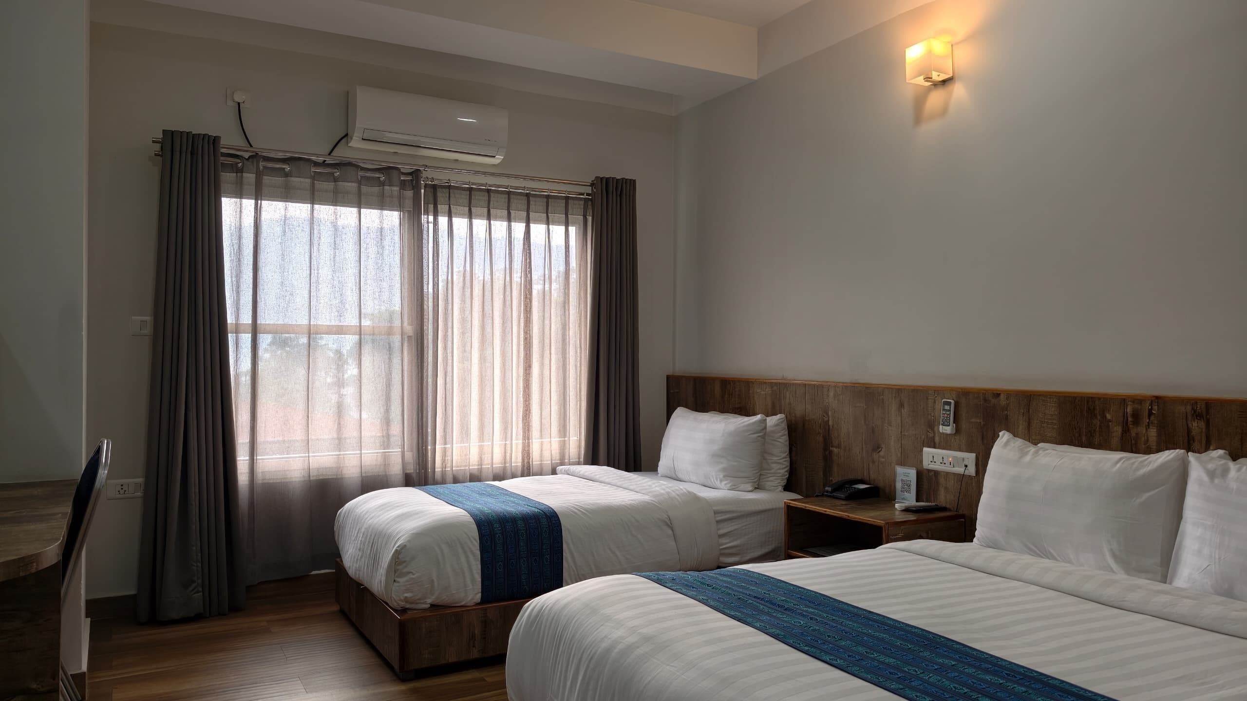 Camera d'albergo con due letti, una testiera in legno, un comodino con il telefono e una finestra con tende.