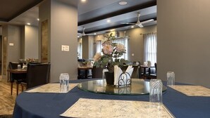 Un comedor con una mesa redonda de cristal, mantel azul oscuro y un jarrón con flores.