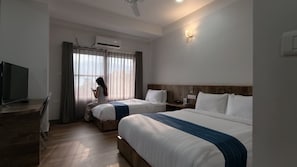 A hotel room with two beds, a desk with a television, and a window with curtains.