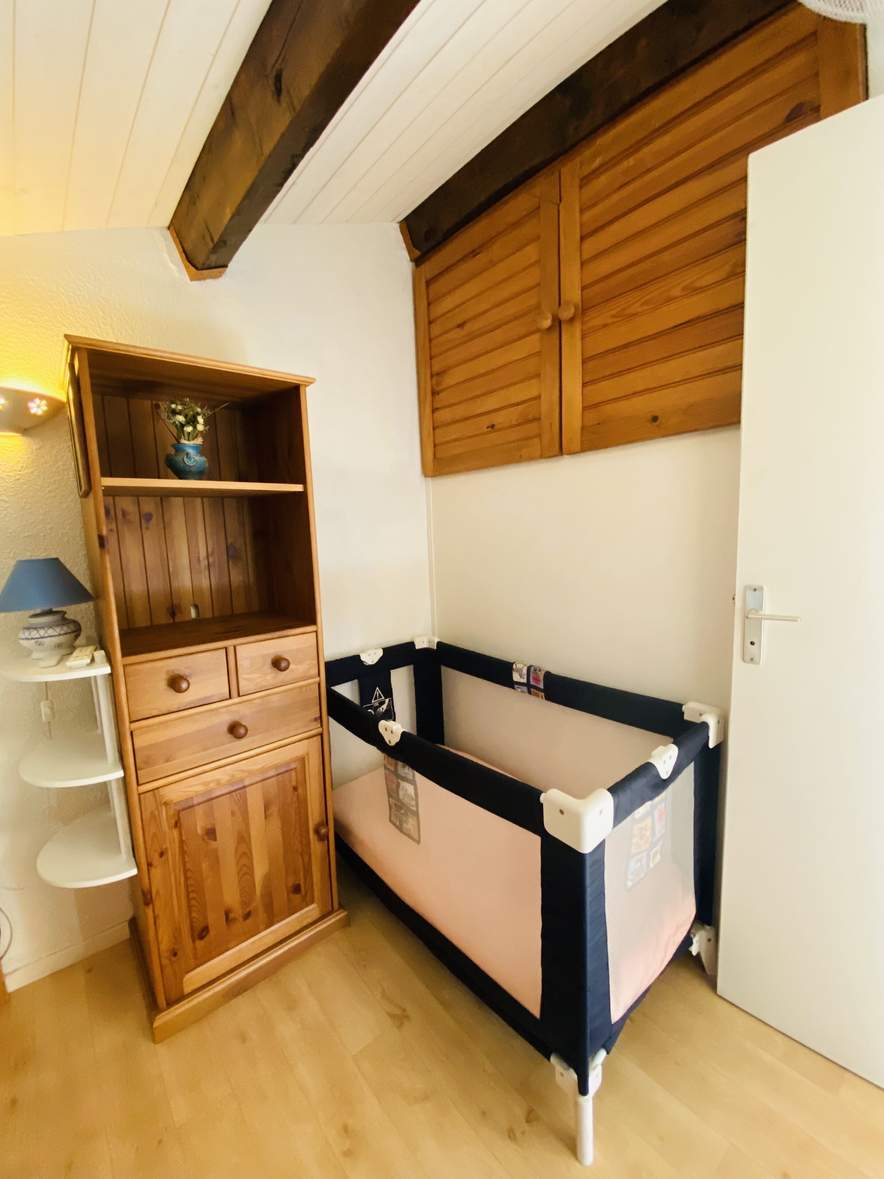 A room with a wooden cabinet, a baby crib, and a wooden door.