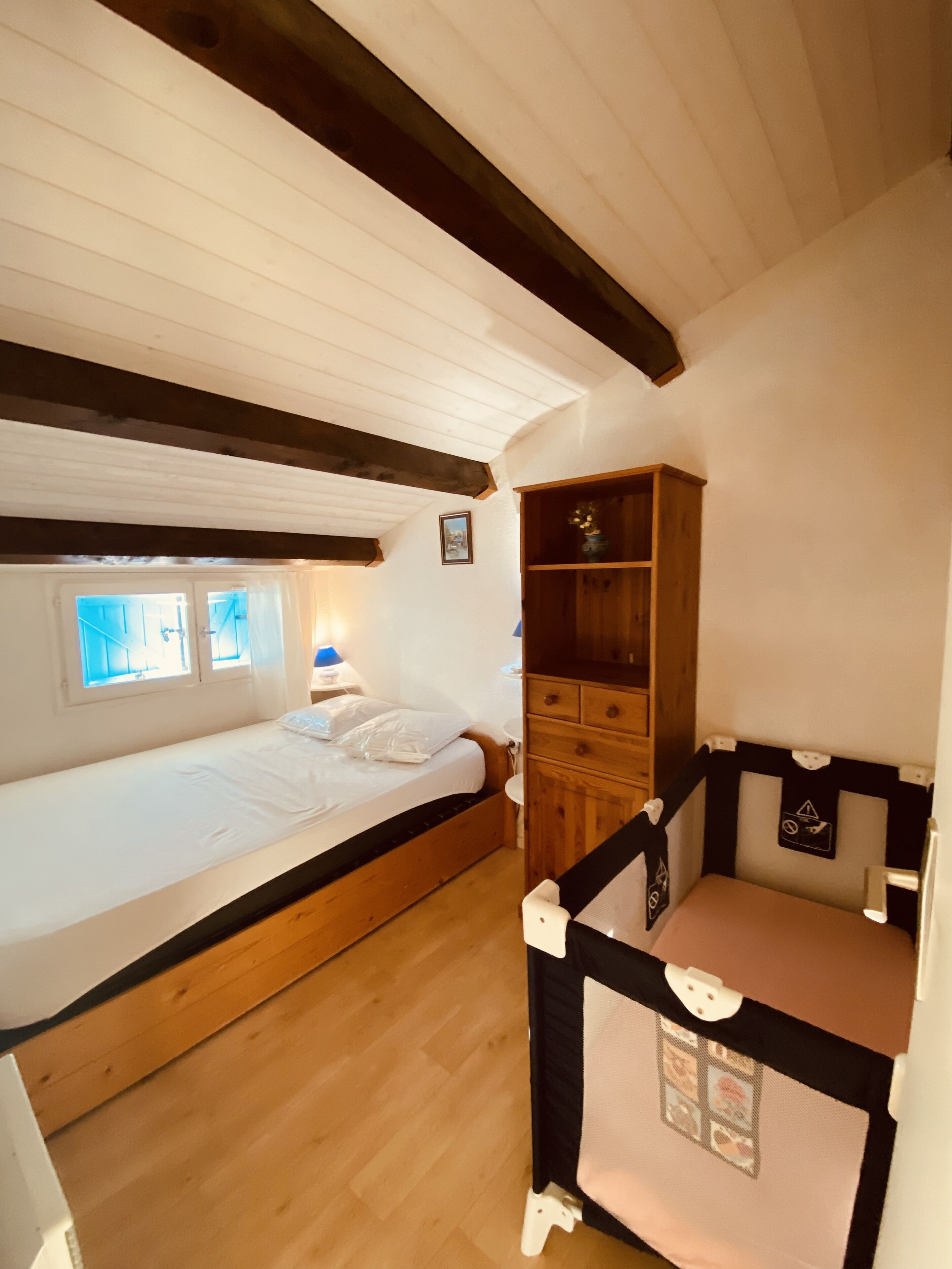Une chambre avec un lit simple, une armoire en bois et un petit coin bureau.