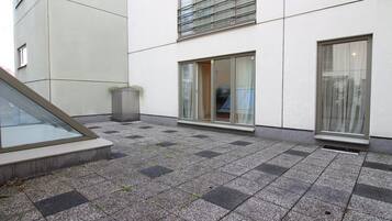 Ein Gebäudefassaden mit bepflastertem Untergrund, einem Mülleimer und einem Fenster mit Vorhang.
