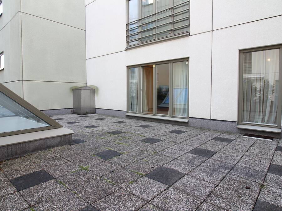 Ein Gebäudefassaden mit bepflastertem Untergrund, einem Mülleimer und einem Fenster mit Vorhang.