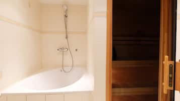 A bathroom with a bathtub, a shower, and a wooden door leading to another room.