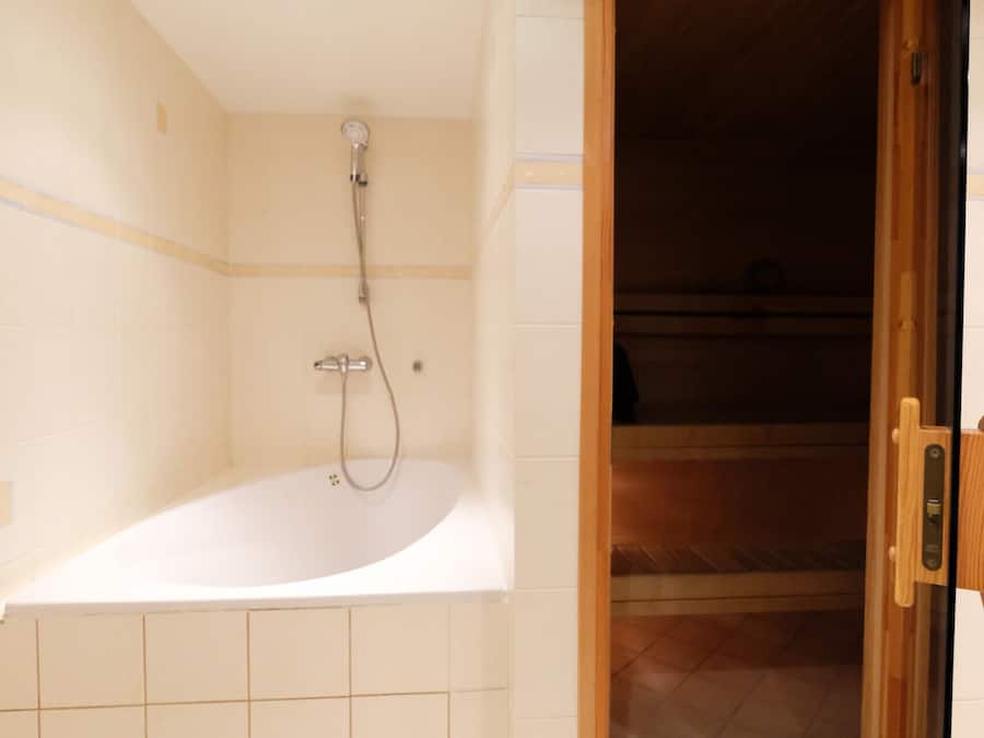 A bathroom with a bathtub, a shower, and a wooden door leading to another room.