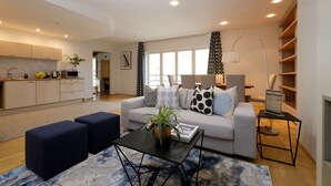 A modern living room with a sofa, coffee table, and ottomans. There is a kitchen area with cabinets and a sink. - Tallinn City Apartments Roosikrantsi (Tallinn)