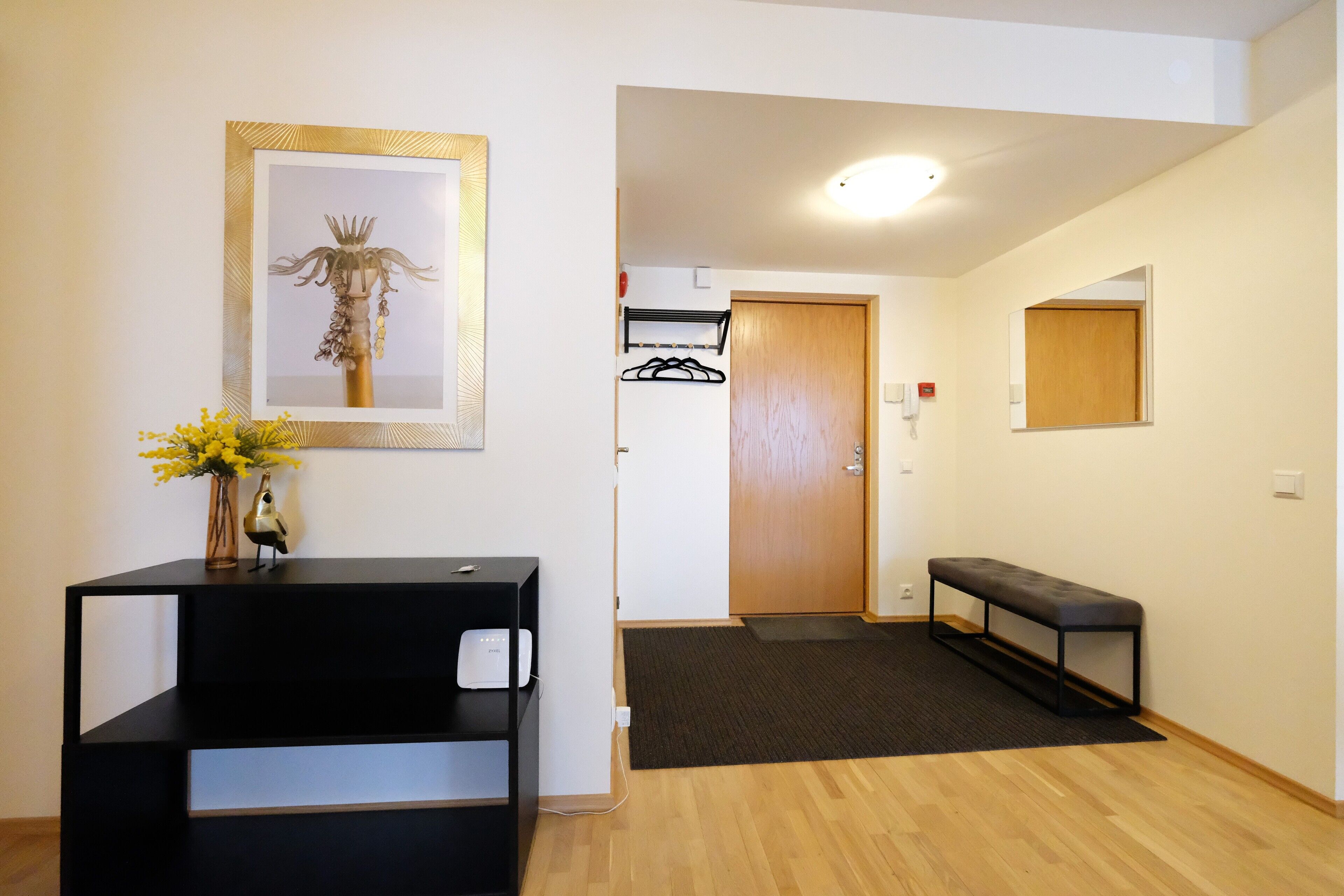 Zona de recepción con un mostrador negro, una obra enmarcadas, un banco y una puerta que da a otra habitación.