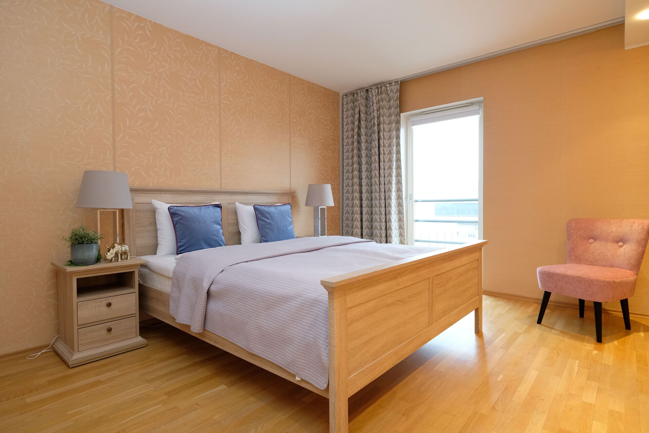 Une chambre à coucher avec un lit en bois, deux tables de chevet, une commode, une chaise et une fenêtre avec des rideaux.