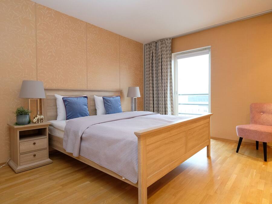 Une chambre à coucher avec un lit en bois, deux tables de chevet, une commode, une chaise et une fenêtre avec des rideaux.