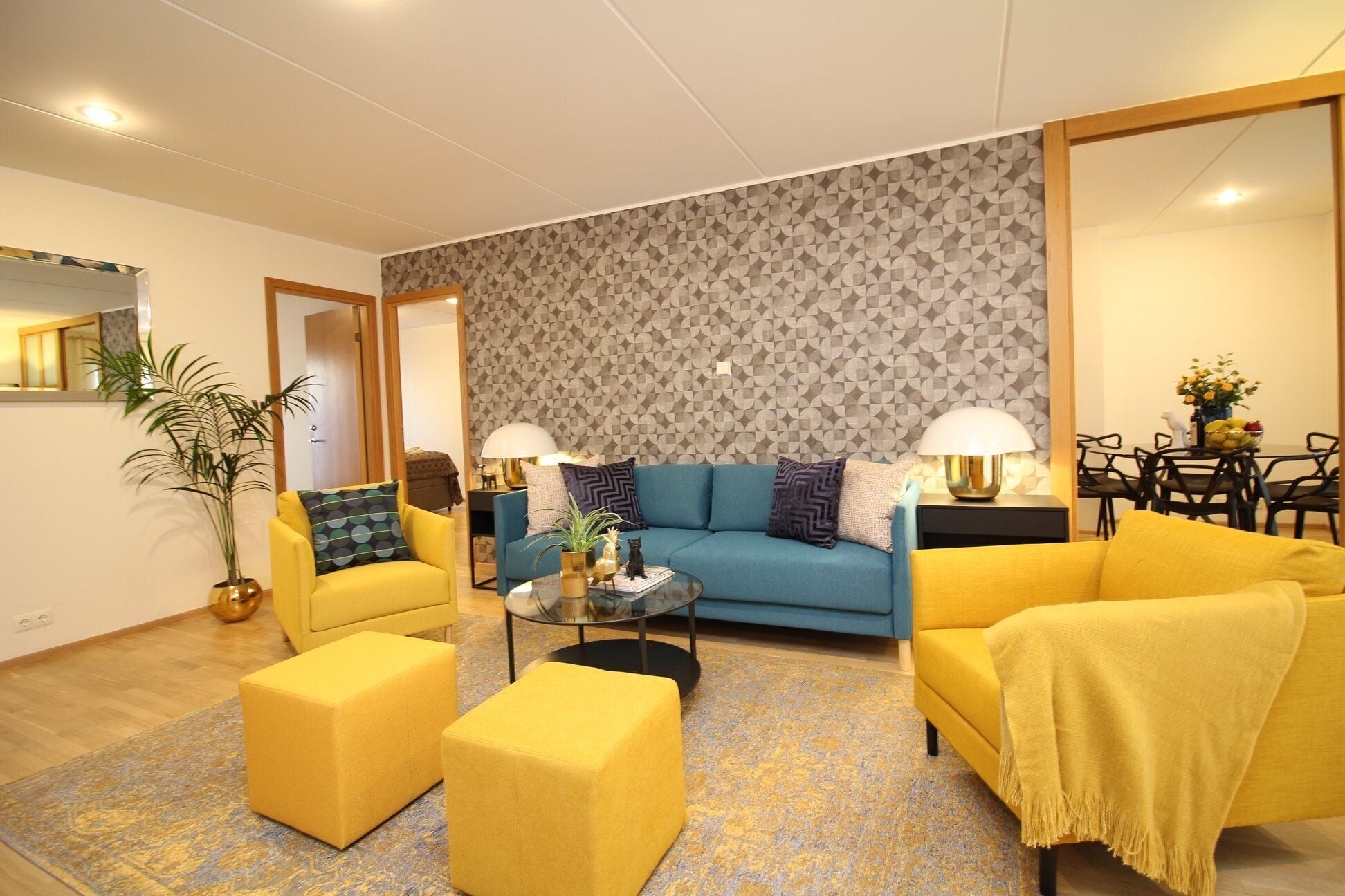 A modern living room with a sofa, two yellow armchairs, a coffee table, and a patterned wall.