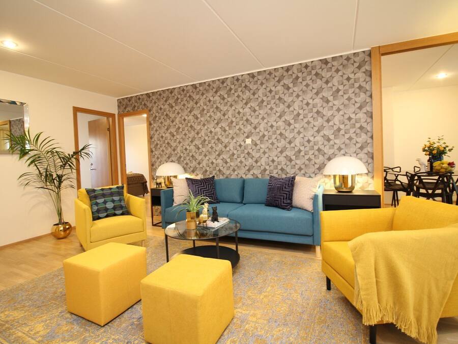 A modern living room with a sofa, two yellow armchairs, a coffee table, and a patterned wall.