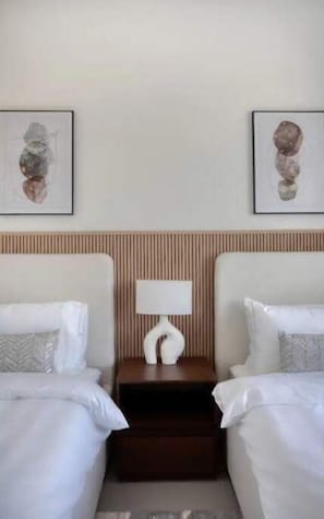 A hotel room with two beds, a nightstand with a lamp, and two wall-mounted artworks. - Luxury Apartment in Dubai (Dubai)