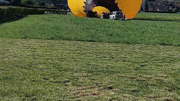Een grote gele luchtballon in een grasveld met bergen op de achtergrond.