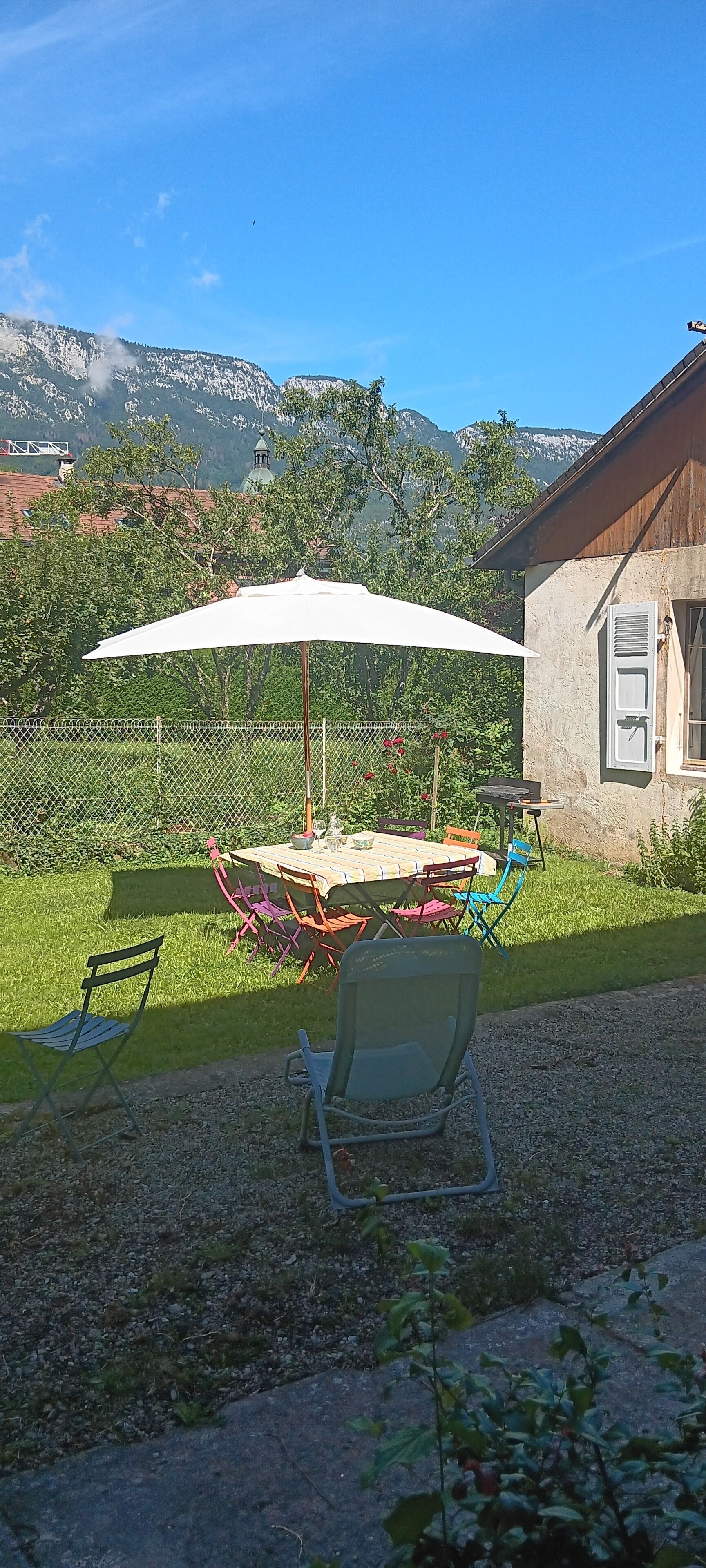 A patio with a table and chairs, a white umbrella, and a view of mountains in the background.