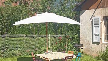 A patio with a table and chairs, a white umbrella, and a view of mountains in the background.