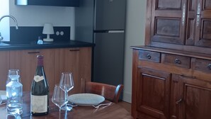A dining area with a wooden table set for four, surrounded by chairs. A wine bottle and glasses are on the table. There is a refrigerator and wooden cabinets in the background. - lac D'annecy Dans Maison de Charme (Doussard)