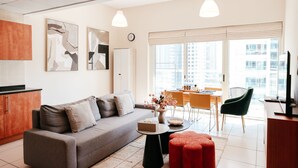 Ein modernes Wohnzimmer mit grauem Sofa, einem kleinen runden Tisch, roten Hocker und einem Essbereich mit gelbem Tisch und Stühlen.