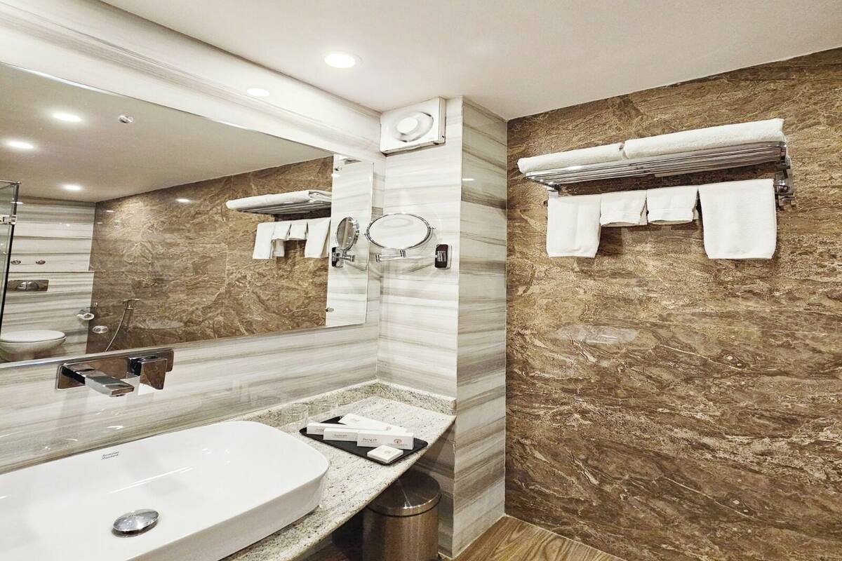 A modern bathroom with a large mirror, a sink, a shower, and a towel rack.