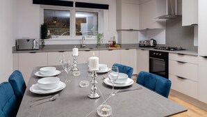 A modern kitchen with a dining table set for four, featuring white plates, glasses, and candles.