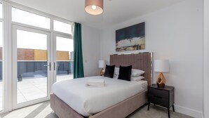 A modern hotel room with a large bed, a view through glass doors, and a painting on the wall.