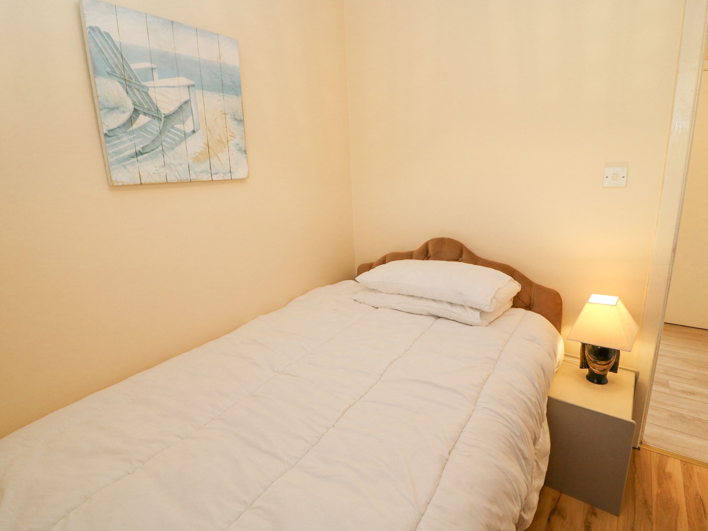 Un dormitorio con cama, mesita de noche, lámpara y un cuadro en la pared.