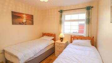 A bedroom with two single beds, a nightstand with a lamp, a window with curtains, and a painting on the wall.