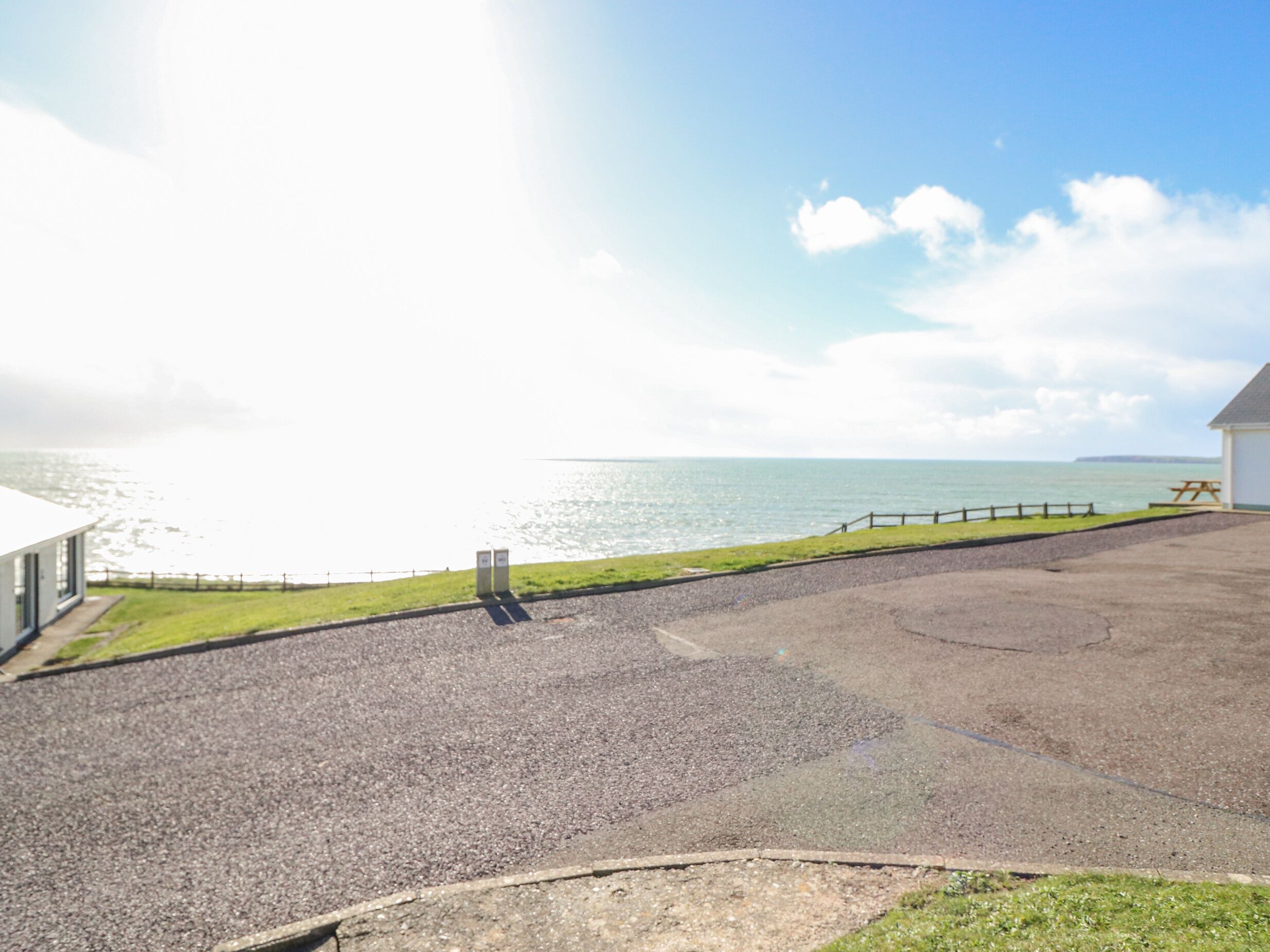 A coastal view with a paved area, a picnic table, and a building with a white roof.