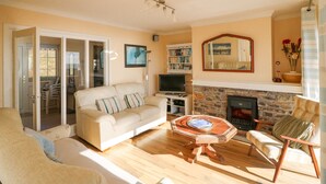 A living room with a sofa, armchair, and a coffee table. There is a fireplace, a bookshelf, and a TV. - Sea's The Dream (Clonakilty)