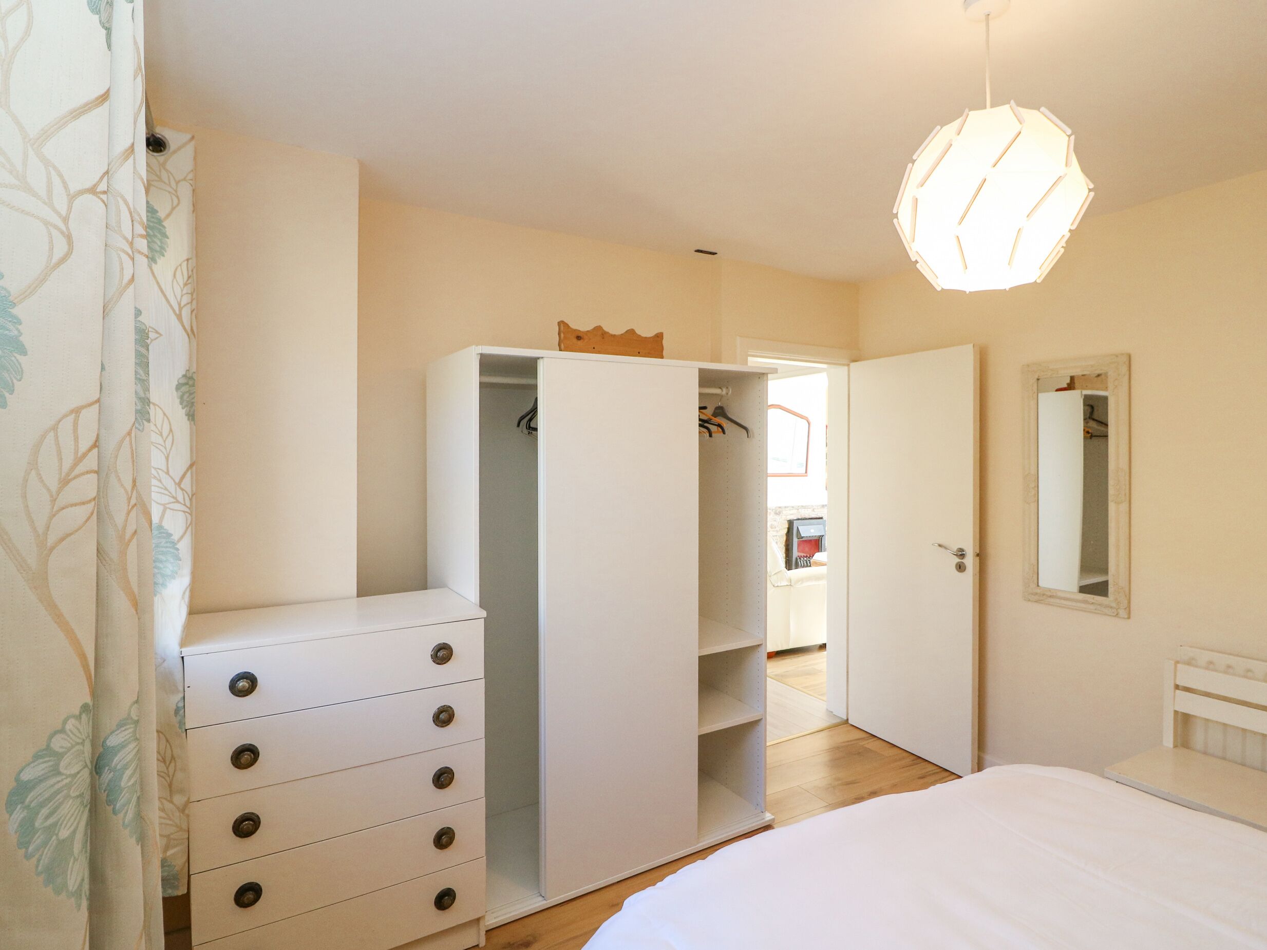 Ein Schlafzimmer mit einem weißen Kleiderschrank, einem Bett, einer Pendelleuchte und einem Spiegel an der Wand.