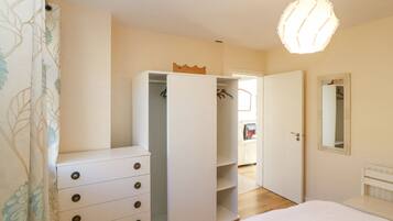Ein Schlafzimmer mit einem weißen Kleiderschrank, einem Bett, einer Pendelleuchte und einem Spiegel an der Wand.