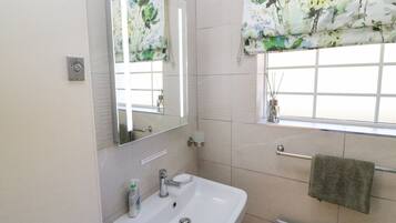 Ein Badezimmer mit einem weißen Waschbecken, einem Spiegel, einem Fenster mit Blumenmuster-Jalousie und einem Handtuchhalter.