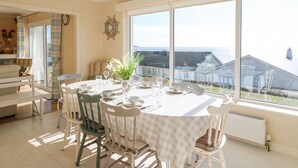 A dining area with a table set for six, large windows offering a view of the sea, and a cozy seating area with a sofa and chairs. - Sea's The Dream (Clonakilty)