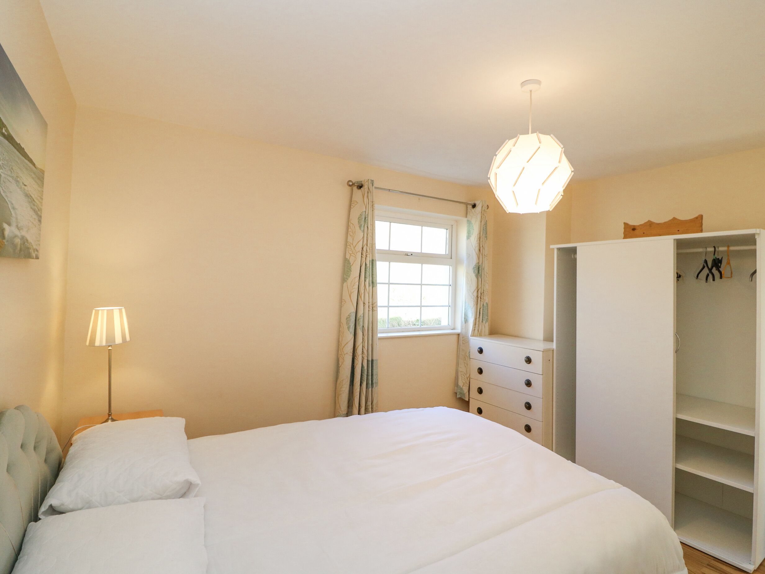 A bedroom with a bed, a bedside lamp, a wardrobe, and a window with curtains.
