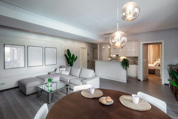 A modern living room with a sectional sofa, a dining table with placemats, and a kitchen in the background. - Florissa (Blevio)