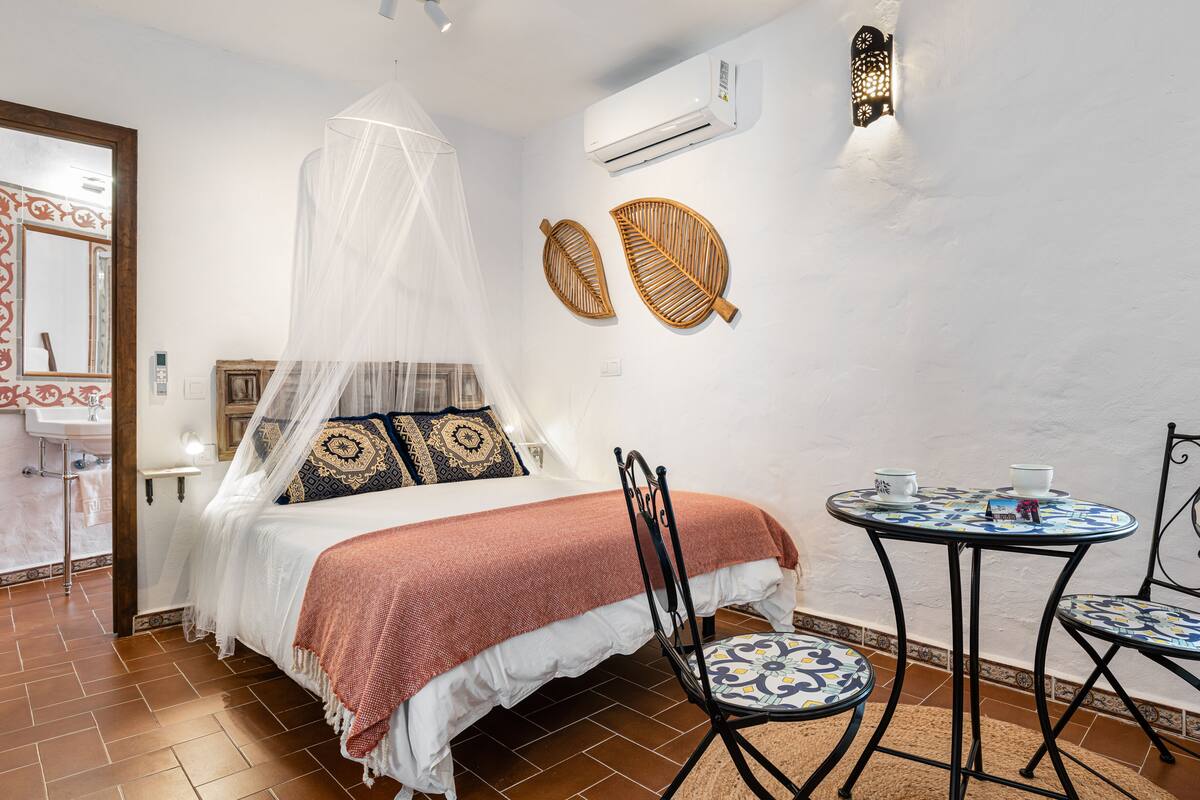 Une chambre à coucher comprenant un lit, une table de chevet, une chaise, une petite table ronde et un climatiseur fixé au mur.