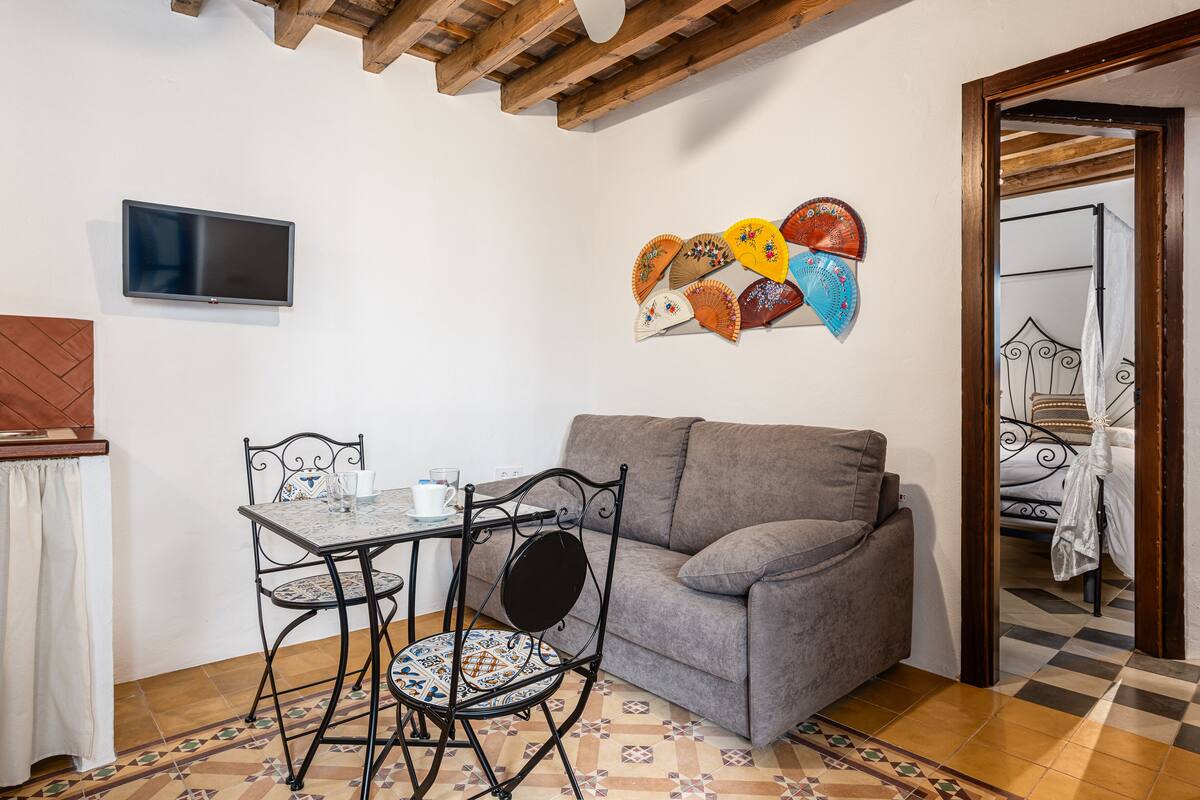 Une pièce chaleureuse avec un canapé, une petite table entourée de chaises, un téléviseur à écran plat et un mur décoré de motifs de ventilateurs.
