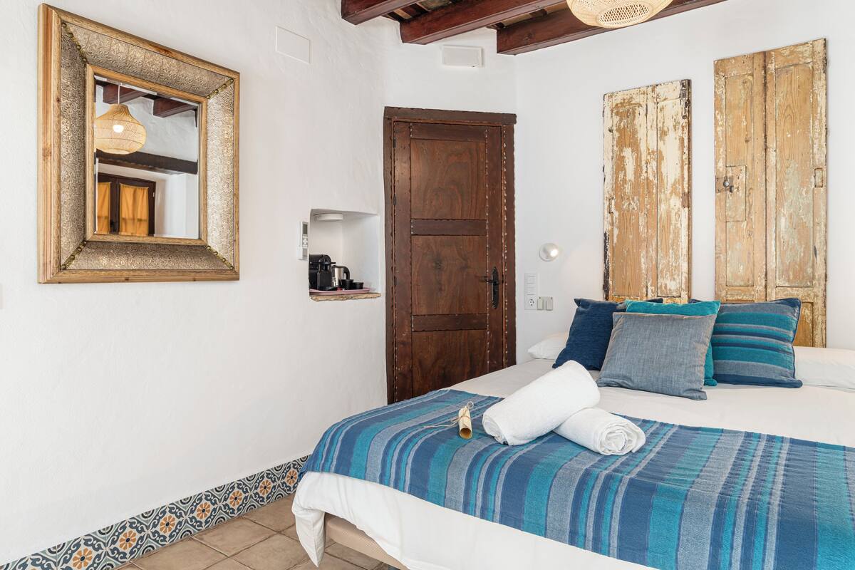 Une chambre à coucher avec un lit, une porte en bois, un miroir et une étagère sur laquelle se trouve une machine à café.