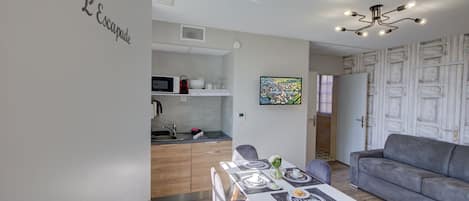 A modern living room with a grey sofa, a dining table set for two, and a kitchen area with a microwave and sink.
