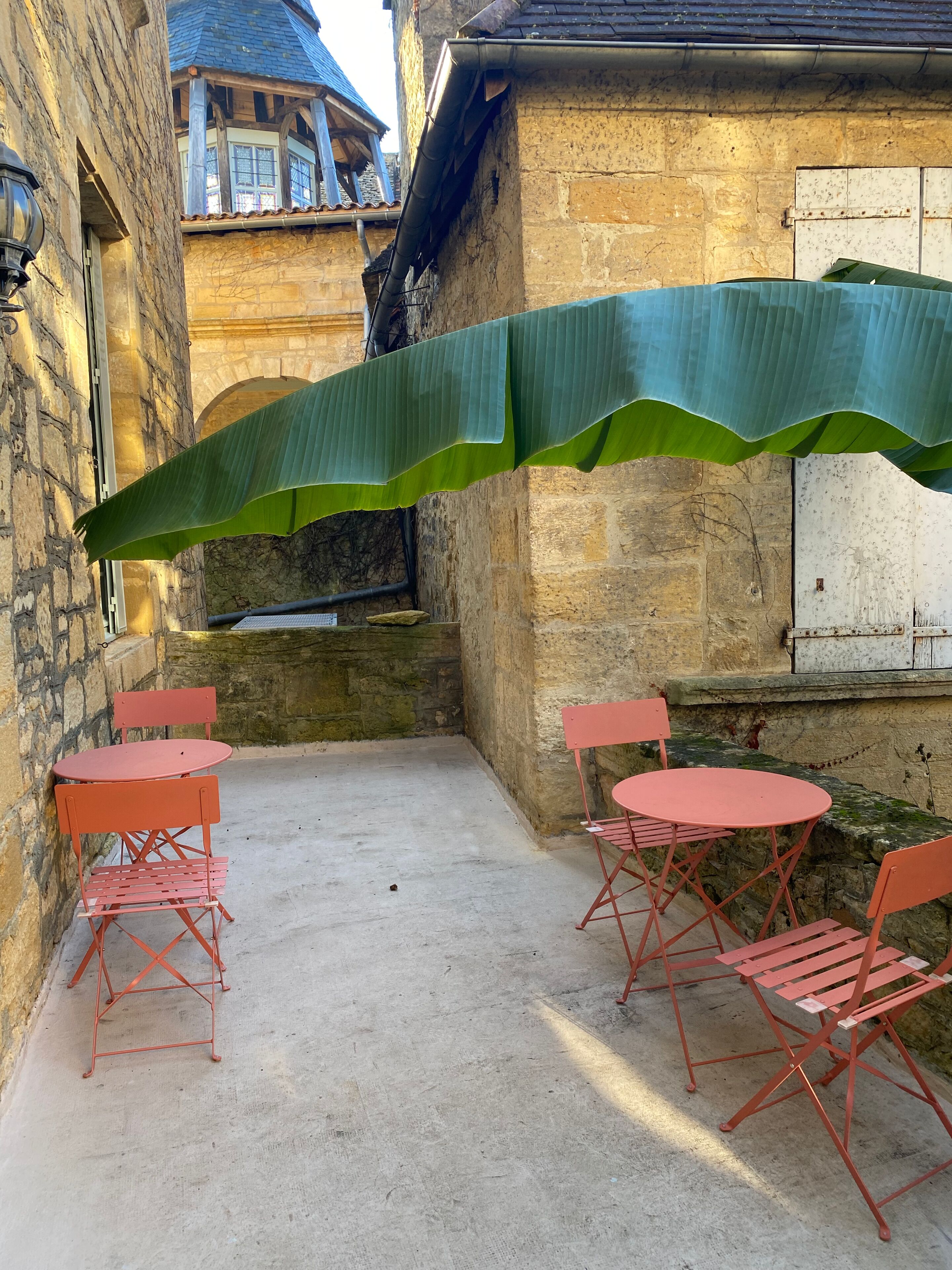 Patio esterno con sedie e tavoli in metallo rosso, un muro in pietra e un ombrellone verde.