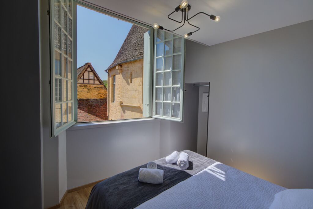 A bedroom with a large window, a bed with a dark headboard, and a towel on the bed.