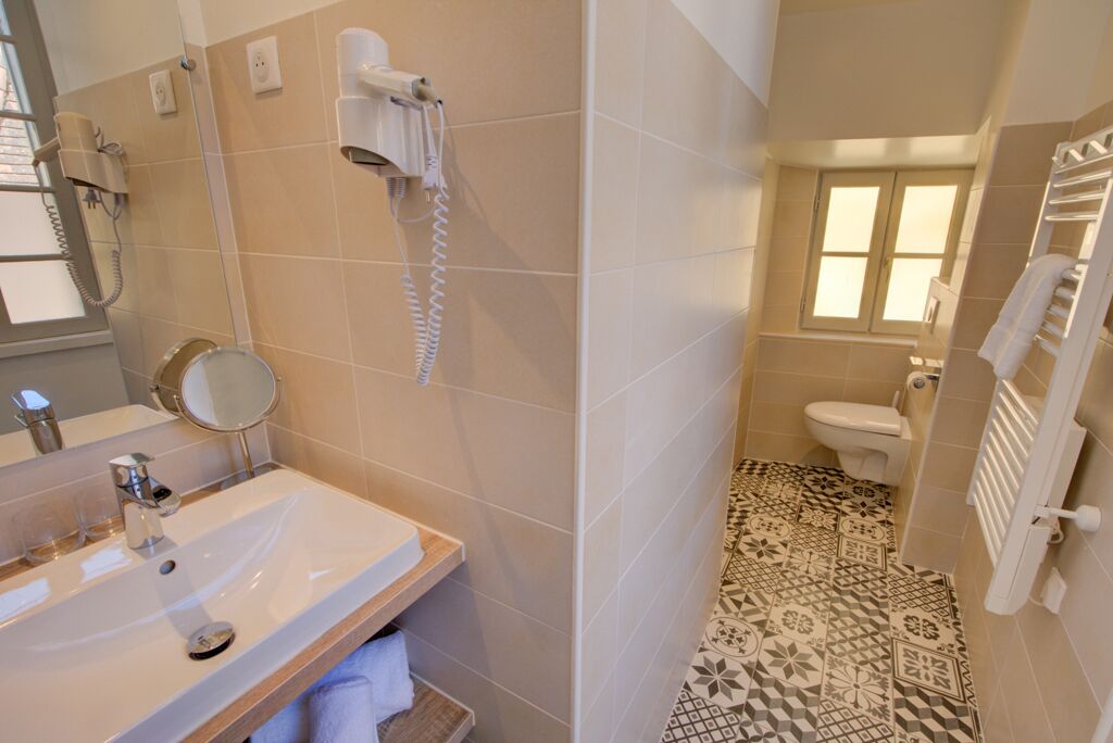 A bathroom with a sink, mirror, hairdryer, and toilet.