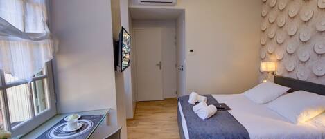 A hotel room with a bed, a desk with a chair, a window with curtains, and a wall with a circular pattern.