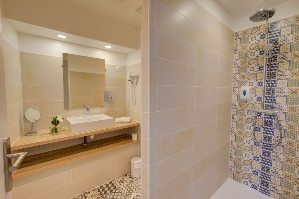 Un baño moderno con tocador de madera, un espejo grande, ducha con pared de azulejos decorativos y piso estampado.