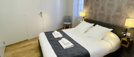 A modern bedroom with a large bed, a small chair, and a nightstand with a lamp.