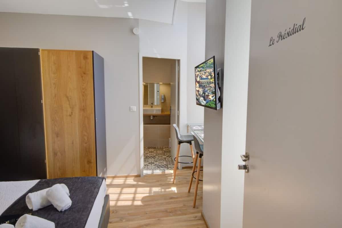 Een slaapkamer met een bed, een houten garderobe, een bureau met stoel, en een badkamer die door een open deur zichtbaar is.