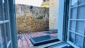 Una habitación con pared de piedra, una ventana que da a una pared de piedra y un edificio, y una mesa con mantel individual que dice "Bon APPETIT! ENJOY Best for you!".